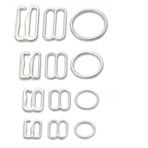 Op de afbeelding: Vier sets zilveren metalen bh-bandverstellers en ringen. Elke set bevat een haak- en oogsluiting, een schuifregelaar en een ring.