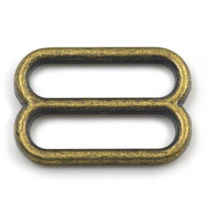 May include: Antique gold metal slider buckle with two loops. The buckle is designed for use with straps or belts.