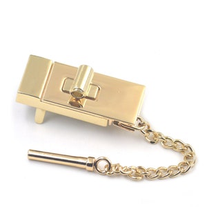May include: Gold-toned metal clasp with a chain and a key. The clasp has a rectangular shape with a small, round keyhole.