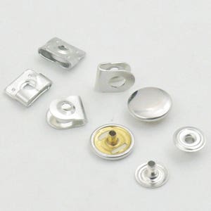 May include: Assortment of silver metal snap fasteners and buttons. The fasteners are in various shapes and sizes. The buttons are round and have a silver finish.