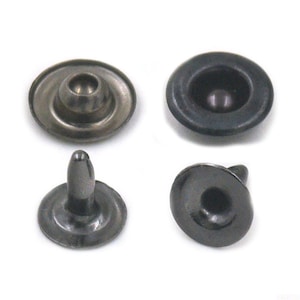 May include: Four dark gray metal snap fasteners. Two are assembled, showing the cap and the post, and two are disassembled. The fasteners have a rounded cap and a post with a rounded tip. The fasteners are for clothing or leather goods.