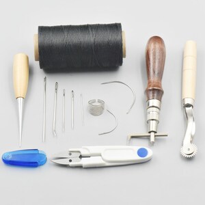 Peut inclure: Ensemble d'outils de maroquinerie avec une bobine de fil ciré noir, un poinçon, des aiguilles, un dé à coudre, un chevalet à piquer, un chanfreineur et une roulette à piquer.