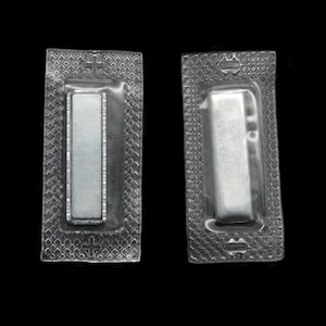 May include: Two clear plastic blister packs with silver foil inserts. Each pack has a cross symbol at the top and a line at the bottom.