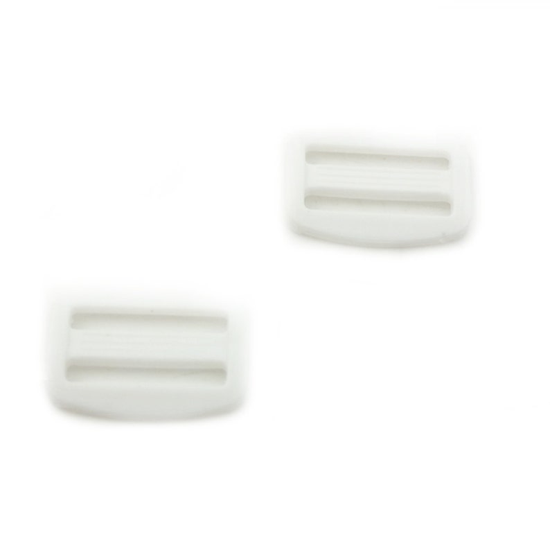 May include: Two white plastic slider buckles. The buckles have two slots for a strap or ribbon.