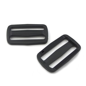 May include: Two black plastic slider buckles. The buckles are rectangular with two slots and a raised centre ridge.