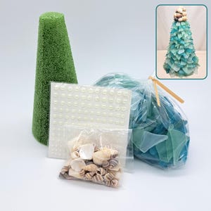 May include: A craft kit containing a green foam cone, a sheet of adhesive white pearl stickers, a small bag of assorted seashells, and a larger bag of blue and teal sea glass pieces, with an inset showing the finished assembled tree structure.