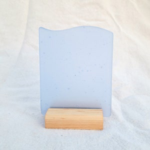 May include: A light blue glass sign with a wavy edge and a wood stand. The glass has a speckled texture.