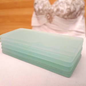 May include: Stack of four frosted glass rectangular coasters in shades of light blue and green.