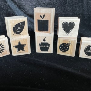 May include: Ten wooden stamps with various designs, including a cupcake, a ladybug, a heart, a star, a leaf, a present, a daisy, and a circle with the text "be happy".