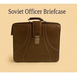 May include: A brown leather briefcase with a handle, clasp, and decorative stitching. The text "Soviet Officer Briefcase" is displayed above the briefcase. The briefcase is rectangular and appears to be vintage.