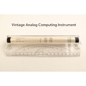 Puede incluir: Instrumento de cálculo analógico vintage con base de plástico transparente y componente cilíndrico. El componente cilíndrico es blanco con tapas negras y marcas impresas. La base tiene marcas de grados y una regla.