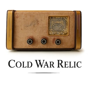 Puede incluir: Radio vintage con cubierta de tela beige, ribetes dorados y tres perillas negras. La radio tiene una pantalla con marco dorado. El texto "Cold War Relic" está debajo.