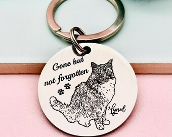 May include: A silver keychain with a round tag engraved with a black and white image of a cat. The tag reads "Gone but not forgotten" with three paw prints below the text. The cat's name "Lyno" is engraved below the image.