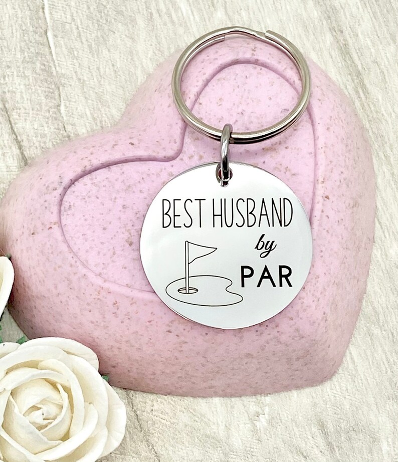 May include: Silver key chain with a round tag that says "Best Husband by Par" with a golf flag and hole graphic.