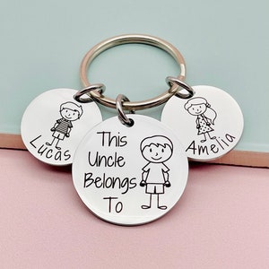 May include: Silver keychain with three round tags. The center tag says "This Uncle Belongs To" and has a stick figure drawing of a boy. The other two tags have stick figure drawings of a boy and a girl and the names "Lucas" and "Amelia" respectively.