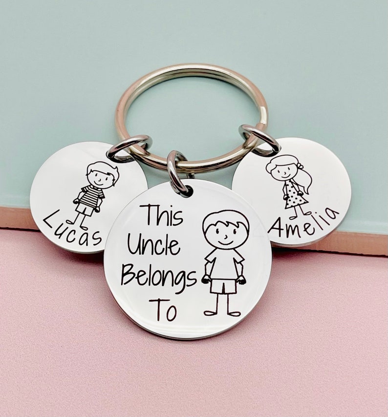 May include: Silver keychain with three round tags. The center tag says "This Uncle Belongs To" and has a stick figure drawing of a boy. The other two tags have stick figure drawings of a boy and a girl and the names "Lucas" and "Amelia" respectively.