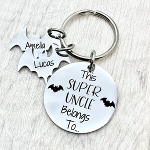 May include: Silver keychain with a round tag that says "This Super Uncle Belongs To..." with two bat silhouettes.  Attached to the keychain are two bat-shaped tags with the names "Amelia" and "Lucas" engraved on them.