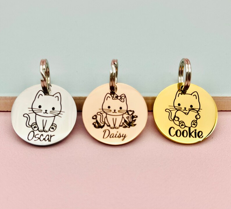 May include: Three round silver, rose gold, and gold pet ID tags with engraved cat illustrations and names "Oscar", "Daisy", and "Cookie".