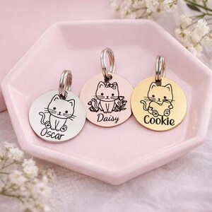 May include: Three circular metal pet ID tags with silver, rose gold, and gold finishes. Each tag features an engraved cat illustration and a name: Oscar, Daisy, or Cookie. Each tag includes a metal split ring for attachment to a collar.