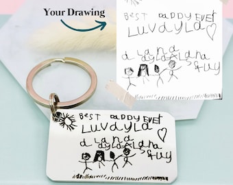May include: A silver rectangular keychain with a drawing and the text "BEST DADDY EVER Luvaylad" in black. A drawing of stick figures and the words "d ay lala na A quy" are also included. A handwritten drawing is taped next to the keychain.