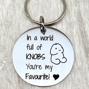 May include: A silver keyring with a round tag that says "In a world full of knobs you're my favourite!" with a small heart icon. The tag also has a cartoon drawing of a knob.