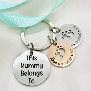 May include: A silver keyring with a round tag that says "This Mummy Belongs To". There are two smaller round tags with footprints and the names "Rose" and "Isla" with their birthdates.