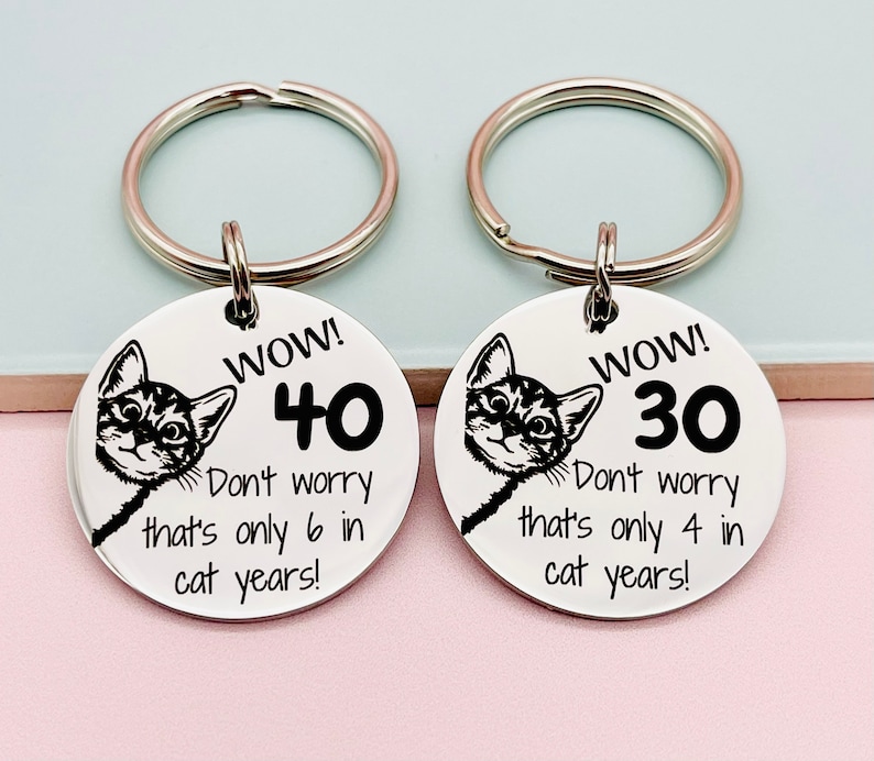 Peut inclure: Deux porte-cl&eacute;s argent&eacute;s avec des &eacute;tiquettes rondes en m&eacute;tal. Chaque &eacute;tiquette repr&eacute;sente un chat de dessin anim&eacute; qui sort d'un c&ocirc;t&eacute; et un num&eacute;ro. L'&eacute;tiquette de gauche indique "WOW! 40 Ne t'inqui&egrave;te pas, ce n'est que 6 ans en ann&eacute;es de chat !" L'&eacute;tiquette de droite indique "WOW! 30 Ne t'inqui&egrave;te pas, ce n'est que 4 ans en ann&eacute;es de chat !"