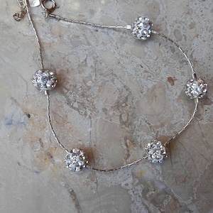 Peut inclure: Un bracelet de cheville en chaîne argentée avec cinq perles rondes incrustées de cristaux blancs.