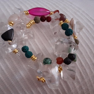 Op de afbeelding: Een armband gemaakt van heldere kwartskristallen, zwarte, rode en groene stenen en gouden draad.