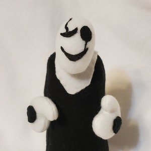 May include: A black and white plush toy with a smiling face and a single black eye. The toy has white arms and hands with black circles on them.