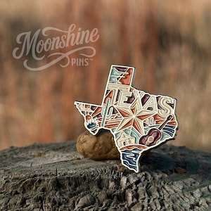 May include: A metal enamel pin shaped like the state of Texas, featuring the word TEXAS in bold letters, a large central star, a guitar, a cactus, and a mission building. The design uses a palette of blue, brown, cream, and orange tones.