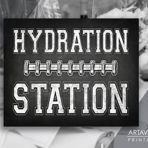 Puede incluir: Un letrero de pizarra negro y blanco con el texto "HYDRATION STATION" en blanco, en negrita, en letra de bloque. El texto está rodeado por una fila de balones de fútbol blancos.
