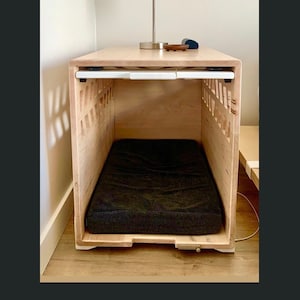 May include: A wooden dog crate with a black bed inside. The crate is on a wooden table with a lamp with an Iron Man comic book themed lampshade.