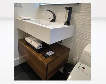May include: A white floating bathroom vanity with a black faucet and a black soap dispenser. The vanity has a wooden cabinet underneath with a black towel rack and a white remote control on top.