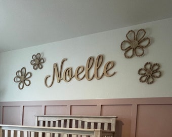 May include: A nursery room with a white cot, a rocking giraffe toy, and a light pink and white rug. The wall is painted a light pink colour and has a wooden sign that says "Noelle" with decorative wooden flowers.