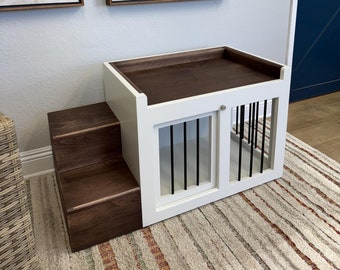 May include: White wooden dog crate with a brown wooden top and steps. The crate has a metal door with vertical bars. The crate is sitting on a striped rug.