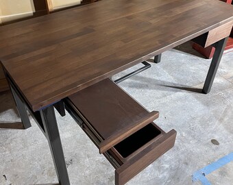 May include: A dark brown wooden desk with a black metal frame and a drawer. The desk has a simple design and is made of high-quality materials.