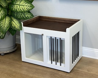 May include: White wooden dog crate with a walnut top and black metal bars. The crate has a door with a small metal handle. The crate is sitting on a wooden floor.