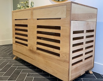 May include: A wooden dog crate with a slatted front and two drawers. The crate is light brown and has a modern design. It is sitting on a black and white tiled floor.