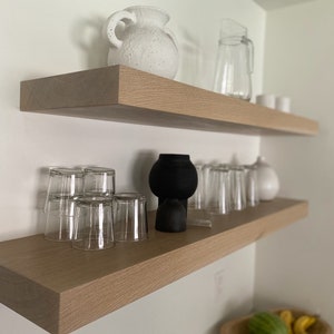 Könnte beinhalten: Zwei Holzregale mit einer weißen Keramikvase, einem durchsichtigen Glaskrug und einer schwarzen Keramikvase mit Glasbechern im unteren Regal.