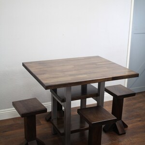May include: A square wooden table with a metal frame and four matching wooden stools. The table has a dark brown finish and the stools have a slightly lighter brown finish. The table has a shelf underneath the tabletop.