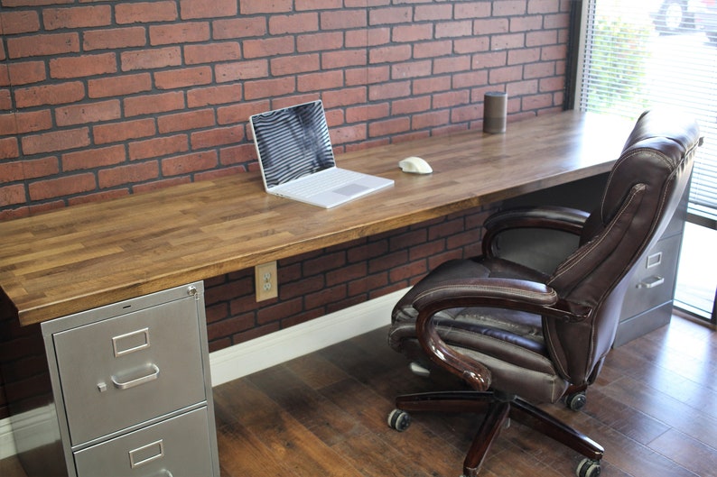 May include: A wooden desk with a metal file cabinet and a brown leather office chair. A laptop computer is on the desk with a white wireless mouse.
