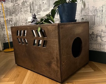 May include: A dark brown wooden cat litter box with a round opening and a rectangular front panel with multiple square cutouts. The litter box is sitting on a light wood floor.