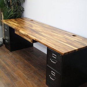May include: A black metal desk with two sets of drawers and a wood top. The desk has a natural wood finish with a variety of wood tones. The desk is sitting on a wood floor.
