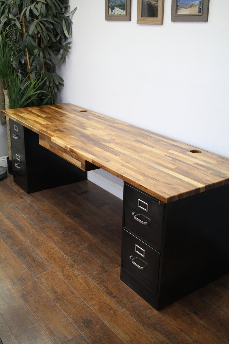 May include: A black metal desk with two sets of drawers and a wood top. The desk has a natural wood finish with a variety of wood tones. The desk is sitting on a wood floor.