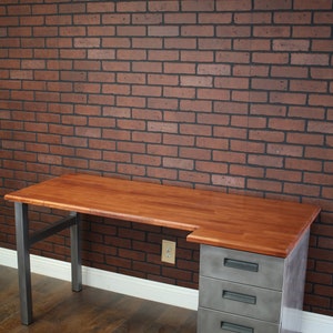 May include: A wooden desk with a metal frame and three drawers. The desk has a light wood top and a dark metal frame. The drawers are made of metal and have a brushed finish.