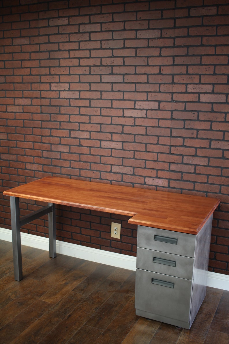 May include: A wooden desk with a metal frame and three drawers. The desk has a light wood top and a dark metal frame. The drawers are made of metal and have a brushed finish.