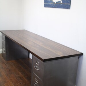 May include: A dark wood desk with two metal drawers on each side. The desk is in a room with a wooden floor and a wall with a blue and white wooden cutout of the United States.