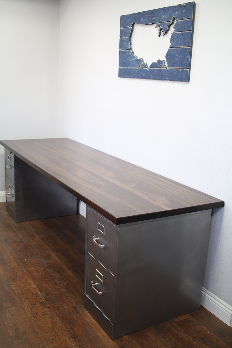 May include: A dark wood desk with two metal drawers on each side. The desk is in a room with a wooden floor and a wall with a blue and white wooden cutout of the United States.