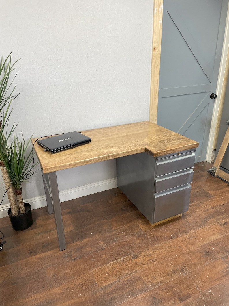 May include: A wooden desk with a metal frame and drawers. The desk has a light wood top and a gray metal base. A laptop computer is on the desk.